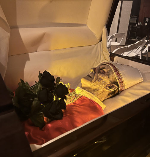 Mannequin dressed as a dead bishop in a casket